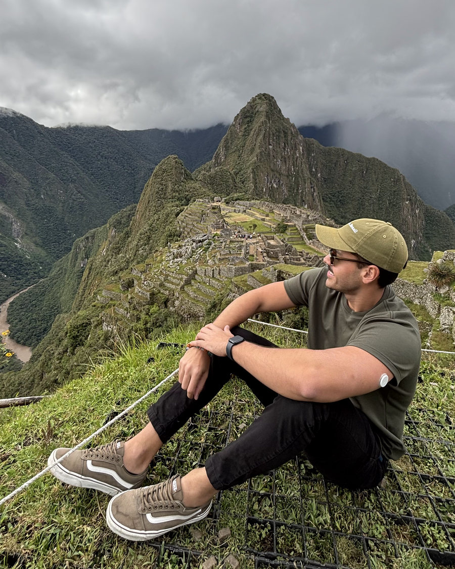 Lucas sentado em Machu Picchu, com o sensor de glicose no braço